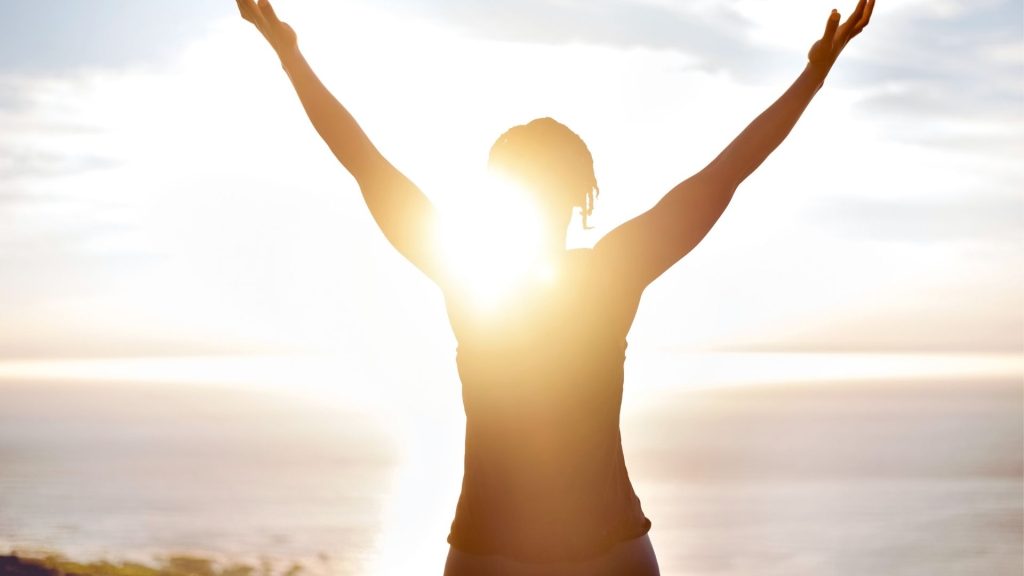 Person standing in sunlight with arms raised, symbolizing hope and stability through methadone treatment and recovery.