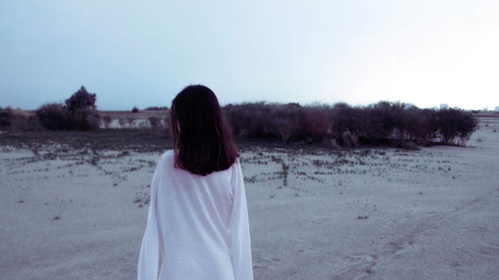 Person standing alone in a barren field representing isolation linked to heroin addiction.