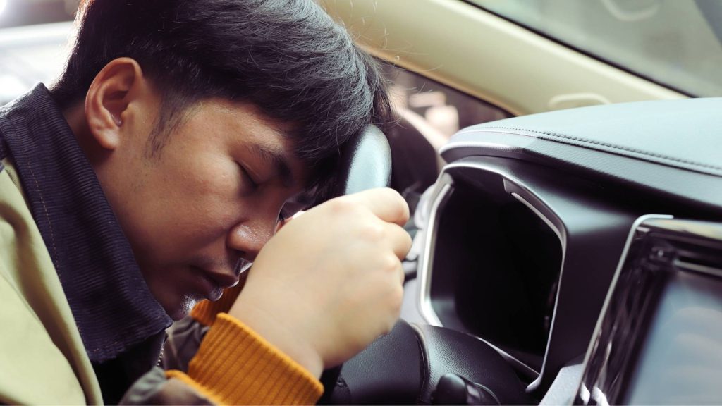 Person slumped over a steering wheel showing extreme drowsiness linked to opioid use.